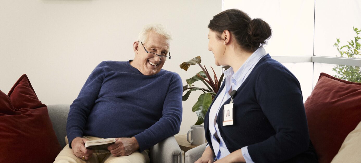 Elderly Male resident laughing with carer sitting on couches